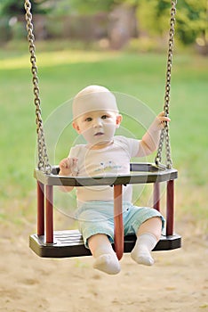 Happy baby boy having fun on a swing ride at a playground