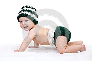 Happy baby boy in knitted hat crawling over white