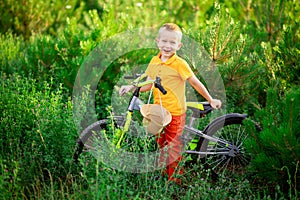 Happy baby boy in orange clothes sitting on a Bicycle in the green grass in summer