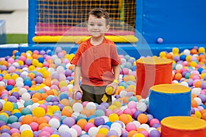 A happy baby boy is playing in a dry pool with colorful balls. Game entertainment center for children. Active leisure.