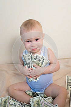 Happy baby boy playing with money, hugging hundreds of dollars