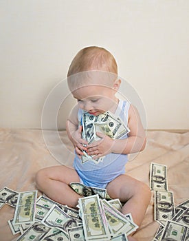 Happy baby boy playing with money, hugging hundreds of dollars