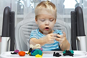 Happy baby boy playing with plasticine. A two-year-old toddler sits in the baby chair and moldes something with a clay photo