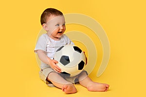 Happy baby boy plays with a soccer ball on a yellow studio background