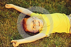 Happy baby boy with red hair in glasses on grass