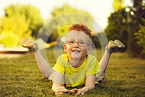 Happy baby boy with red hair in glasses on grass