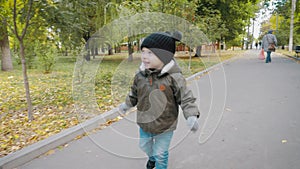 Happy baby boy running in autumnal park. Little child playing on autumn walk. Autumnal forest with golden leaves