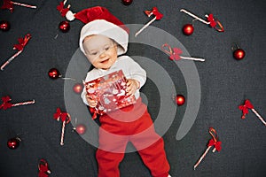 Happy baby boy in Santa Claus hat smiling among festive Christmas candy canes