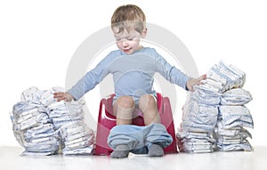 Happy baby boy sitting on chamber pot tearing down diaper piles