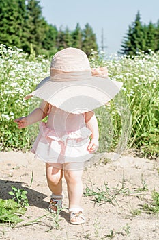 Happy baby boy standing in grass on the fieald with dandelions at sunny summer evening. Smiling child outdoors