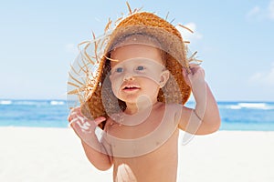 Happy baby boy in straw hat on sunny tropical beach