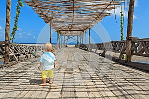Happy baby boy walk by wood bridge to ocean beach