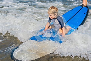 Happy baby boy - young surfer ride on surfboard with fun on sea waves. Active family lifestyle, kids outdoor water sport