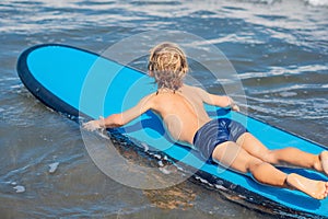 Happy baby boy - young surfer ride on surfboard with fun on sea waves. Active family lifestyle, kids outdoor water sport