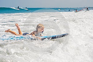 Happy baby boy - young surfer ride on surfboard with fun on sea waves. Active family lifestyle, kids outdoor water sport