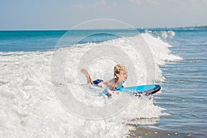 Happy baby boy - young surfer ride on surfboard with fun on sea waves. Active family lifestyle, kids outdoor water sport