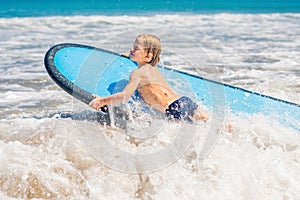 Happy baby boy - young surfer ride on surfboard with fun on sea waves. Active family lifestyle, kids outdoor water sport