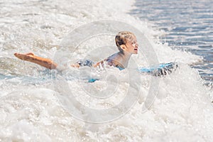 Happy baby boy - young surfer ride on surfboard with fun on sea waves. Active family lifestyle, kids outdoor water sport