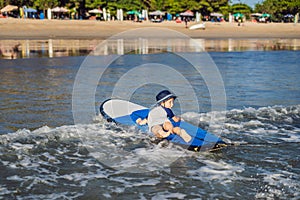 Happy baby boy - young surfer ride on surfboard with fun on sea waves. Active family lifestyle, kids outdoor water sport