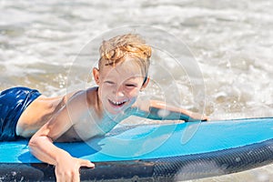 Happy baby boy - young surfer ride on surfboard with fun on sea waves. Active family lifestyle, kids outdoor water sport