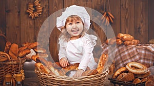 Happy baby chef in wicker basket laughing playing chef in bakery, lots of bread baking.