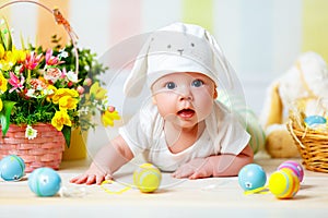 Happy baby child with Easter bunny ears and eggs and flowers