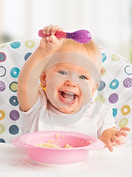 Happy baby child eats itself with a spoon