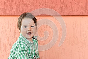 Happy baby on a coral background. Head and shoulders portrait of cute blue-eyed baby girl looking at camera and laughing on a