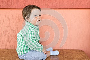 Happy baby on a coral background. Head and shoulders portrait of cute blue-eyed baby girl looking at camera and laughing on a