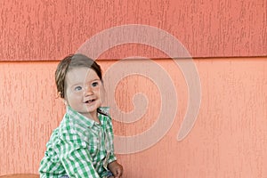 Happy baby on a coral background. Head and shoulders portrait of cute blue-eyed baby girl looking at camera and laughing on a