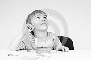 Happy baby dreaming about his own house. Little boy builds small wooden house on table. Child playing with wooden blocks, copy spa