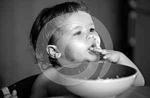 Happy baby eating himself with a spoon. Healthy nutrition for kids. Baby holding a spoon while putting it in his mouth.