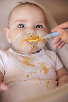 Happy baby eating porridge and smiling in high chair photo