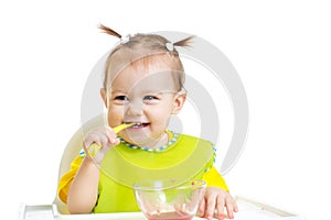 Happy baby eating with spoon sitting at table