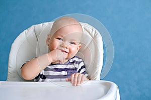 Happy baby. Funny smiling little cutest chubby caucasian white infant child looking at camera on highchair over blue at