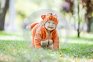 Happy baby girl dressed in fox costume crawling on lawn in park