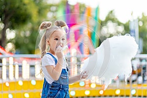 Happy baby girl eating cotton candy at amusement Park in summer