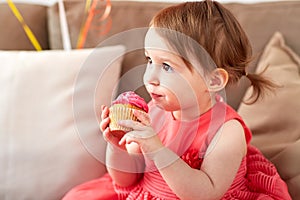Happy baby girl eating cupcake on birthday party