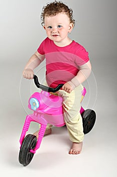 Happy baby girl with her pink bike on grey