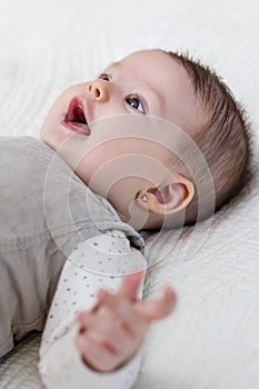 Happy baby girl lying on back over white bedcover