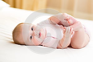 Happy baby girl lying on white sheet and holding her legs