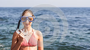 Happy baby girl in mask and snorkel on the beach in summer with sea background