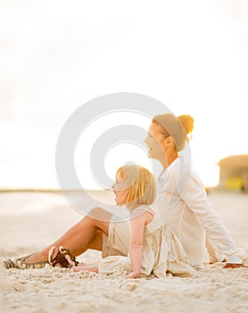 Happy baby girl and mother sitting on the beach