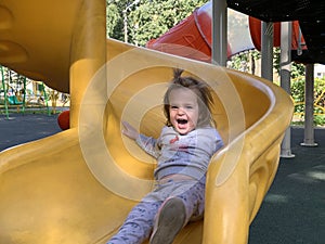 Happy baby girl playing on slide on colorful playground