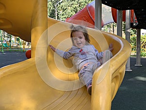 Happy baby girl playing on slide on colorful playground