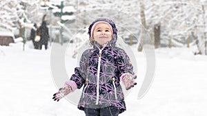 Happy baby girl rejoices in falling snow, Moscow, Russia. Cute little child having fun plays in winter