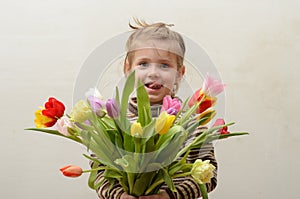 Happy baby girl rejoices and smiles with a bouquet of multi-colored tulips in hands