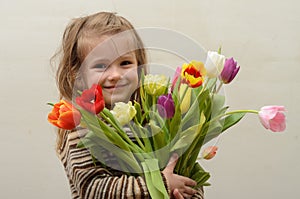 Happy baby girl rejoices and smiles with a bouquet of multi-colored tulips in hands