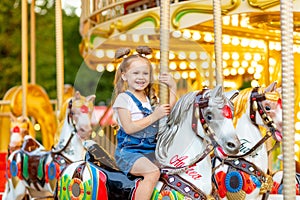 Happy baby girl rides a carousel on a horse in an amusement Park in summer