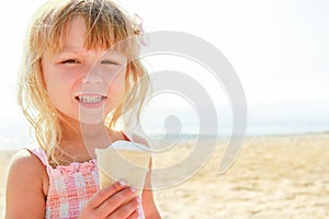 Happy baby girl on the sea in summer eating ice cream outdoors
